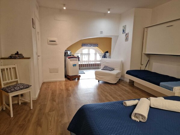 A bedroom with two beds, a white chair, a heater, and a view of a balcony.