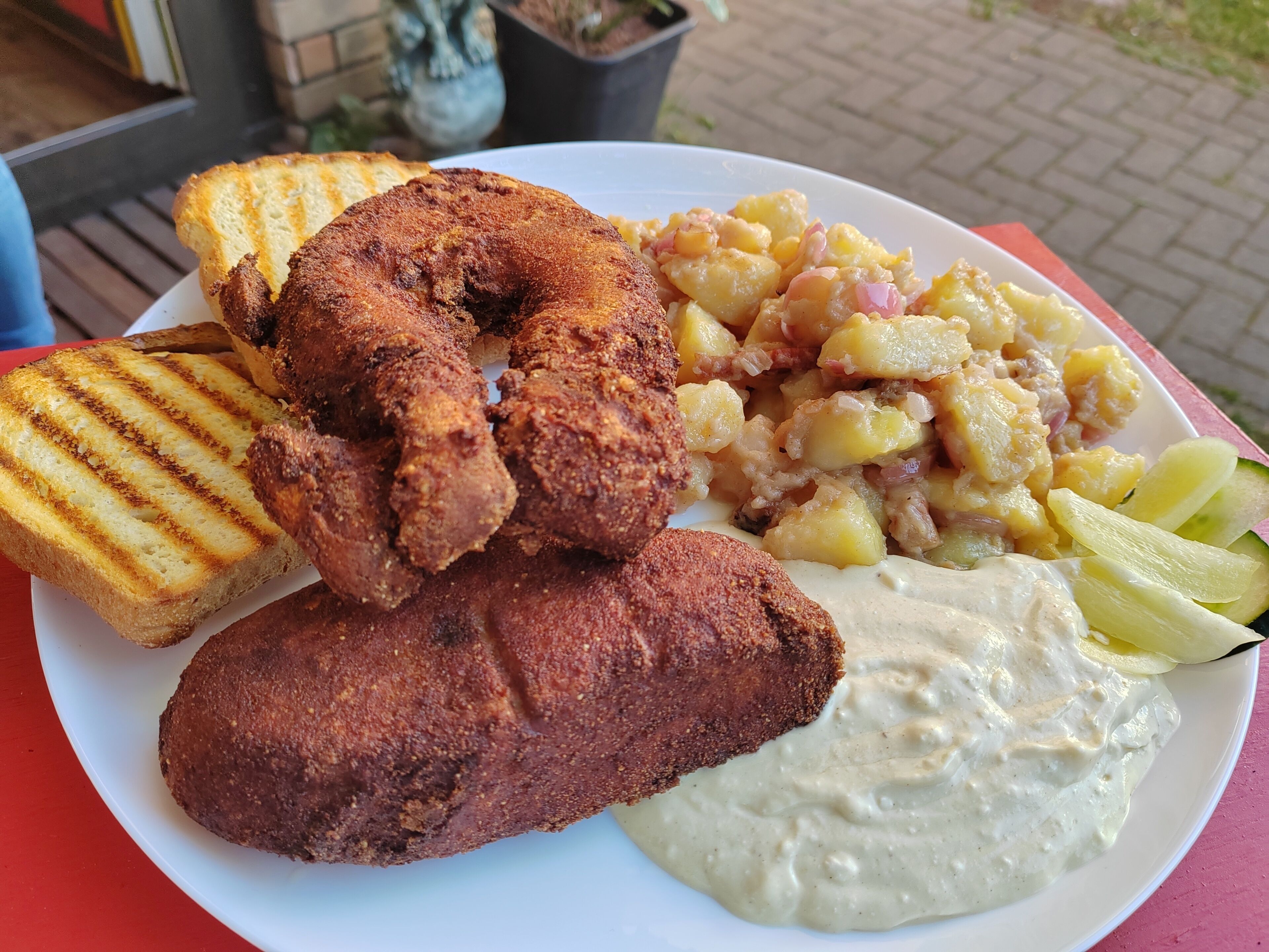 A plate with grilled bread, fried chicken, potato salad, and a creamy sauce.