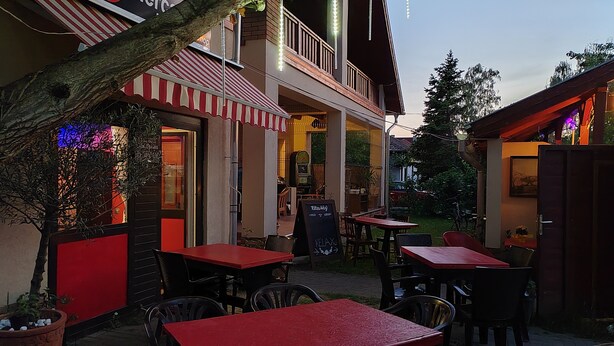 An outdoor seating area with red tables and chairs, a sign for 'de Merces', and a balcony with string lights.