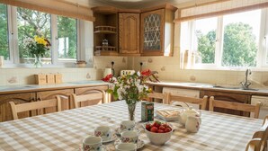 A kitchen with wooden cabinets, a checkered tablecloth, and a dining table set with cups and a bowl of strawberries. - Elmtree Cottage, Cardigan (Cardigan)