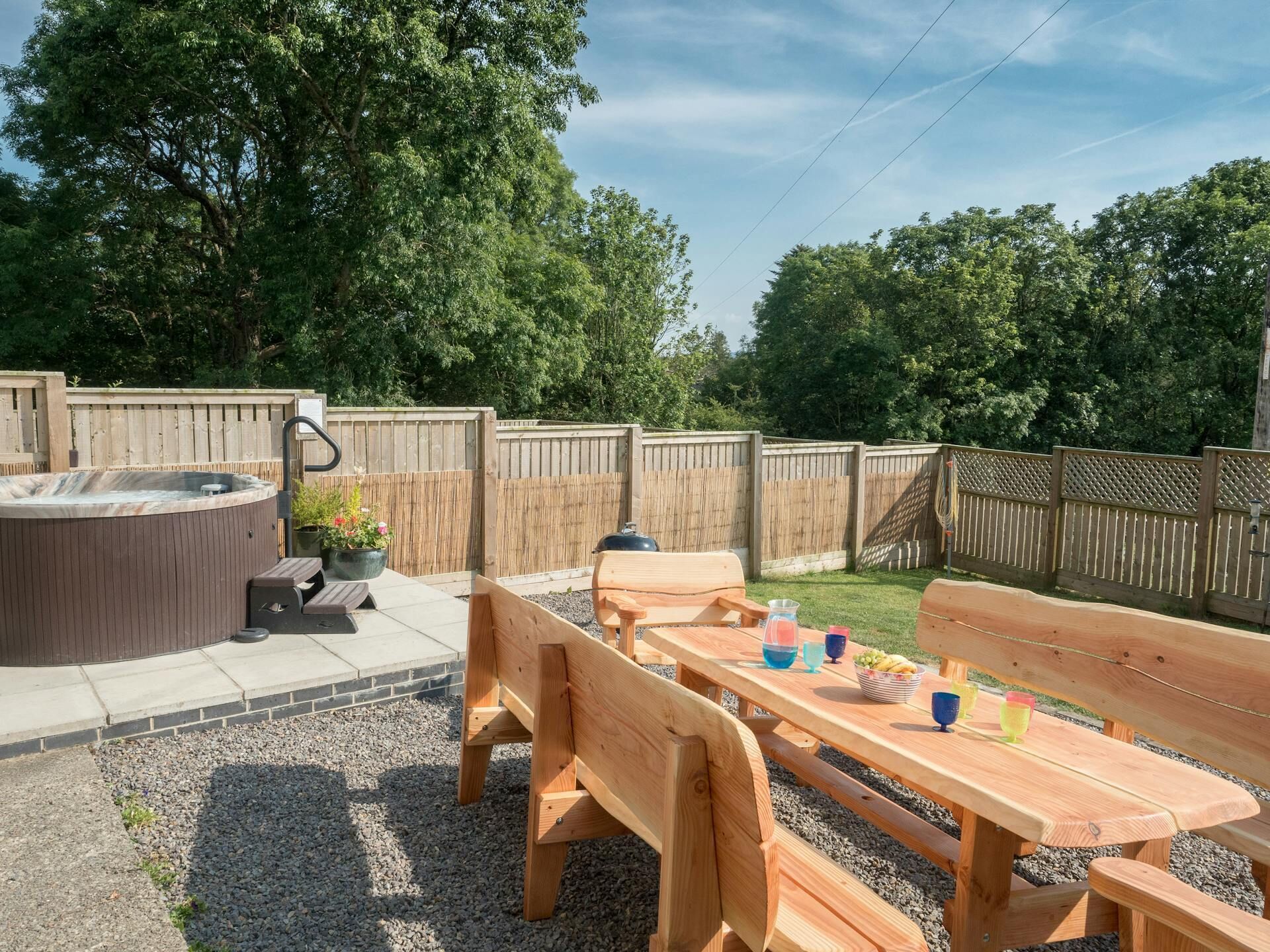 A backyard with a hot tub, wooden deck, picnic table, and barbecue grill.