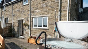 A stone building with a hot tub in the foreground, a wooden bench, and a wooden fence with potted plants. - Elmtree Cottage, Cardigan (Cardigan)