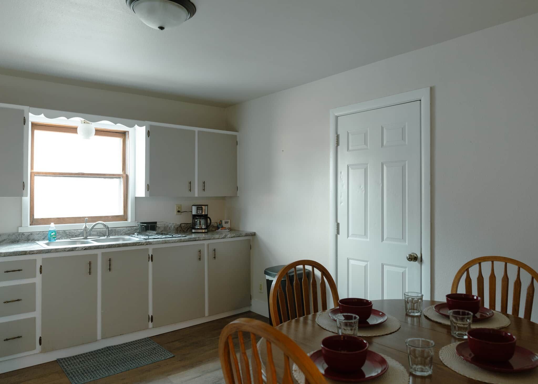 A kitchen with white cabinets, a window, a sink, and a dining table with chairs.