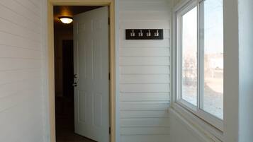 A hallway with a white door leading to a dark room, a window with a view of a snowy landscape, and a wall-mounted light fixture.