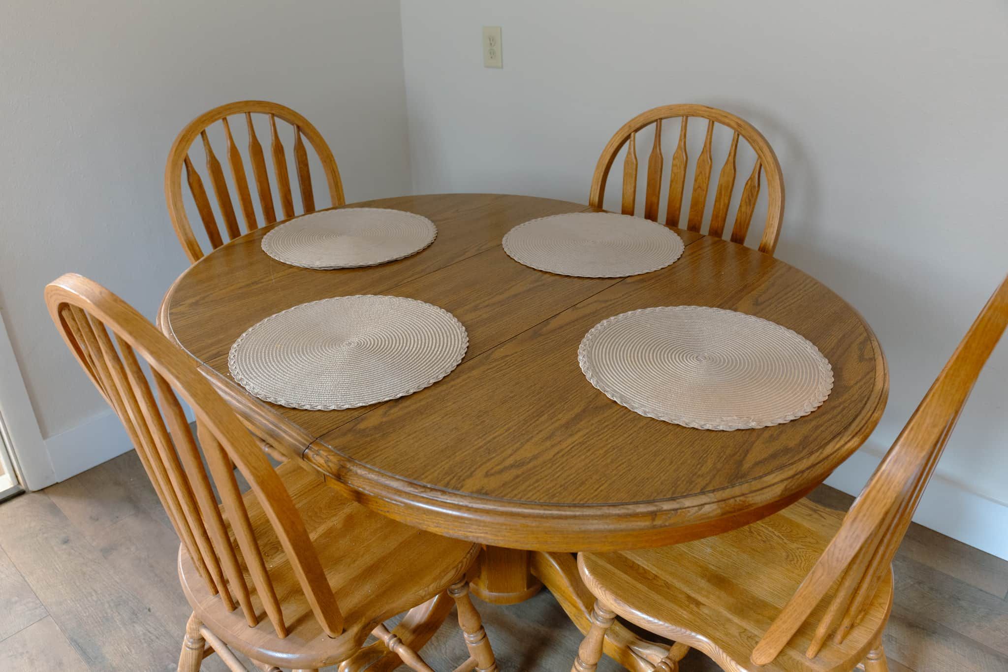 A round wooden dining table with four chairs, each with a woven placemat.
