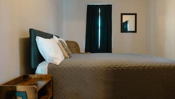 A bedroom with a bed, pillows, a nightstand, a window with curtains, and a framed picture on the wall.