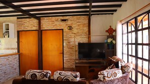 A living room with a TV, patterned sofas, a wooden door, and a stone wall. - FINCA VACACIONAL GUANANI (Socorro)