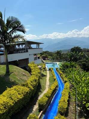 A modern house with a pool, surrounded by lush greenery and a clear view of distant mountains. - FINCA VACACIONAL GUANANI (Socorro)