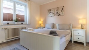 Ein Schlafzimmer mit Bett, Nachttischen, einem Heizkörper und einem Fenster mit Jalousien.