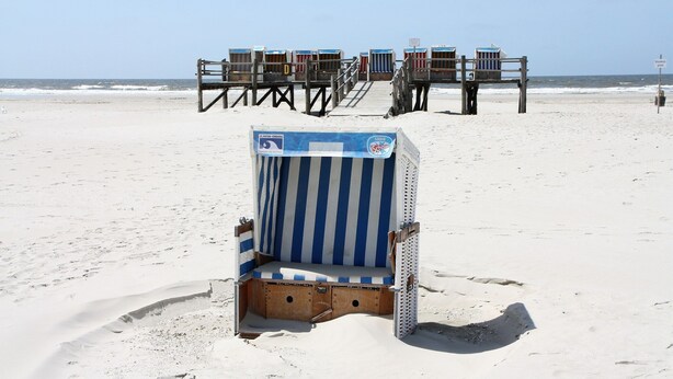 Ein Strand mit einer Reihe gestreifter Liegestühle und einer Holzpromenade, die zu ihnen führt.