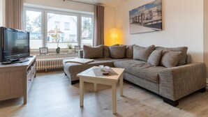 Ein modernes Wohnzimmer mit einer Couch, einem Couchtisch, einem Fernseher und einem Fenster mit Vorhängen.