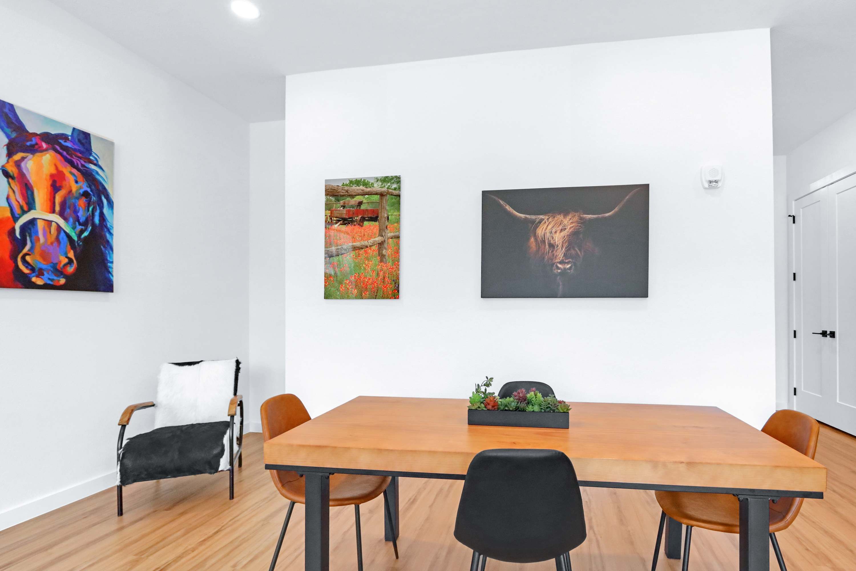 Un espace repas moderne avec une table en bois, des chaises noires et un tableau noir décoré de plantes.