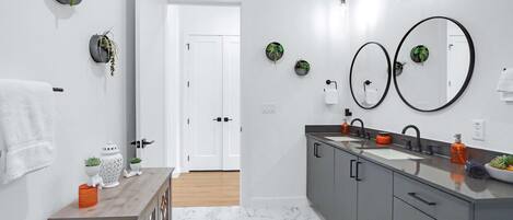 A modern bathroom with a marble floor, a wooden vanity, a double sink, and two large mirrors.