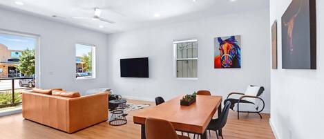 A modern living room with a wooden dining table, a leather sofa, and a TV mounted on the wall.