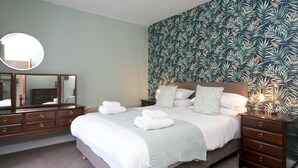 A bedroom with a bed, a dresser, a mirror, and a wall with a tropical leaf pattern. - Llys Owain, comfortable Cottage - Pass the Keys (Amlwch)