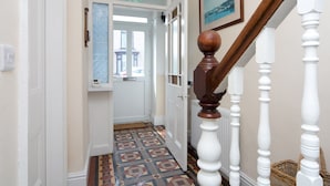 A hallway with patterned flooring, a wooden staircase with white balusters, and a door leading to a room with a view. - Llys Owain, comfortable Cottage - Pass the Keys (Amlwch)