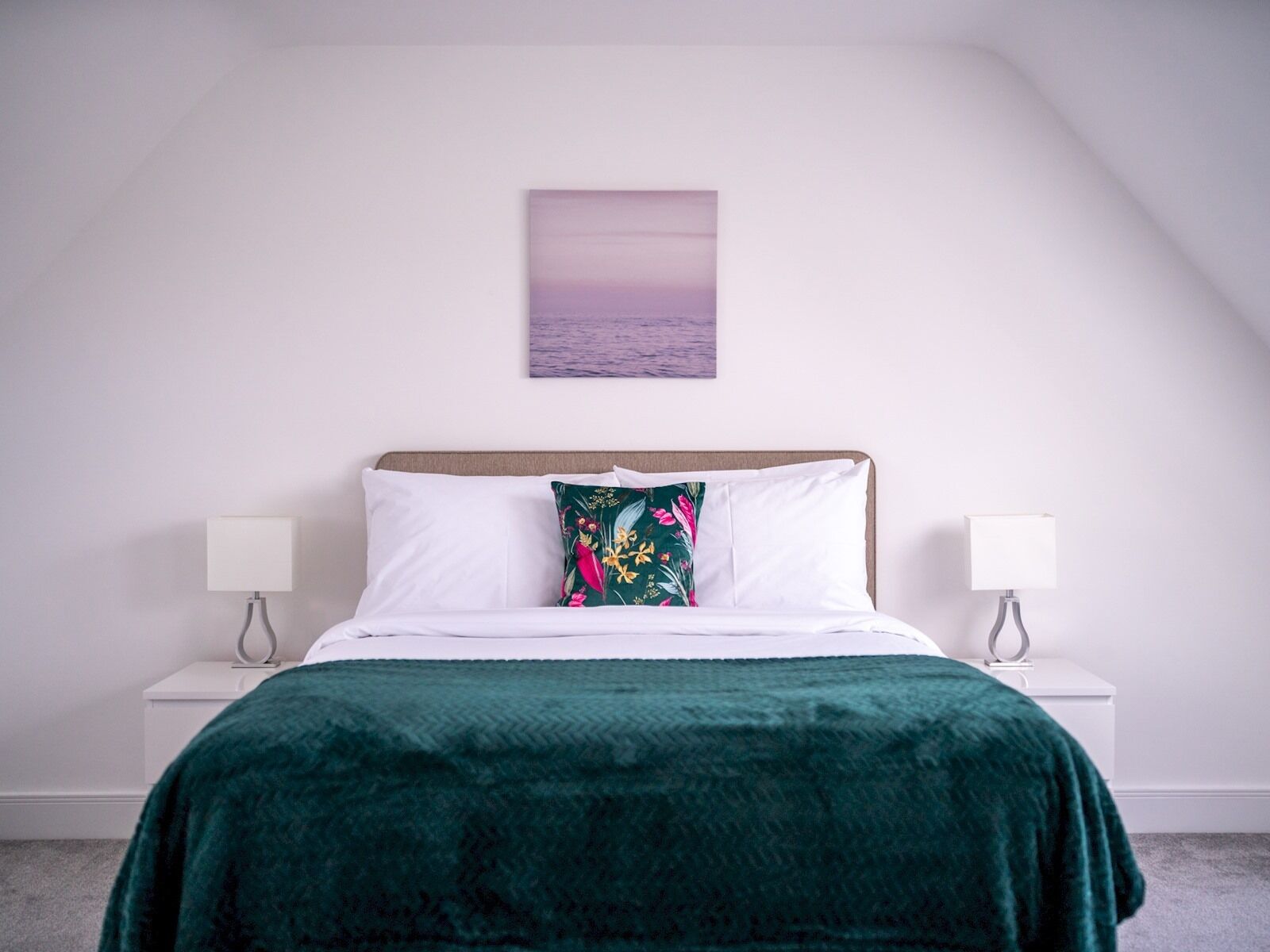 A bedroom with a bed, two bedside tables, and a wall-mounted picture.