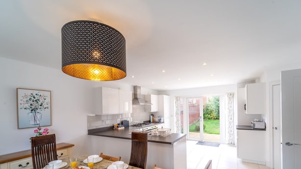 Een moderne keuken met witte kastjes, een centraal eiland en een ontbijtgedeekte eethoek met borden, glazen en croissants.