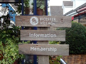 Een houten bord met de aanduidingen 'Bicester Village', 'Informatie' en 'Lidmaatschap'.