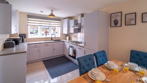 A modern kitchen with a dining area, featuring a stove, sink, and a window with a view of the street. - Shop & Stay at Bicester Village near our 3 Bed Home-  Pass the Keys (Bicester)