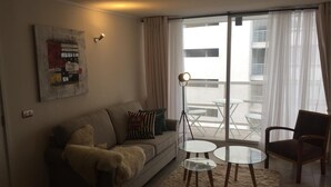 En moderne stue med sofa, sofabord i glas, gulvlampe og udsigt til en altan.
