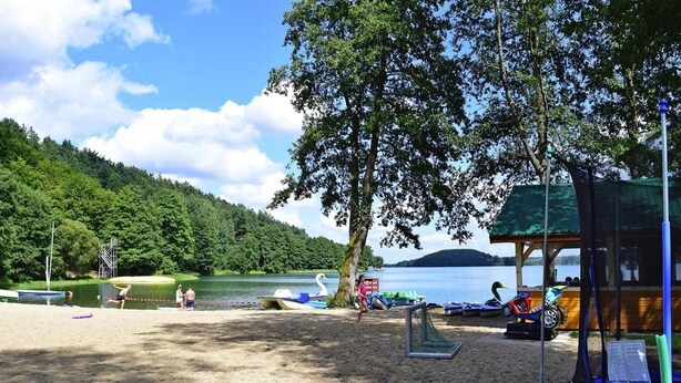 A beach with a sandy area, a lake, boats, and a wooden structure with a roof. - Holiday Home With Fireplace and Private Garden (gmina Stężyca)