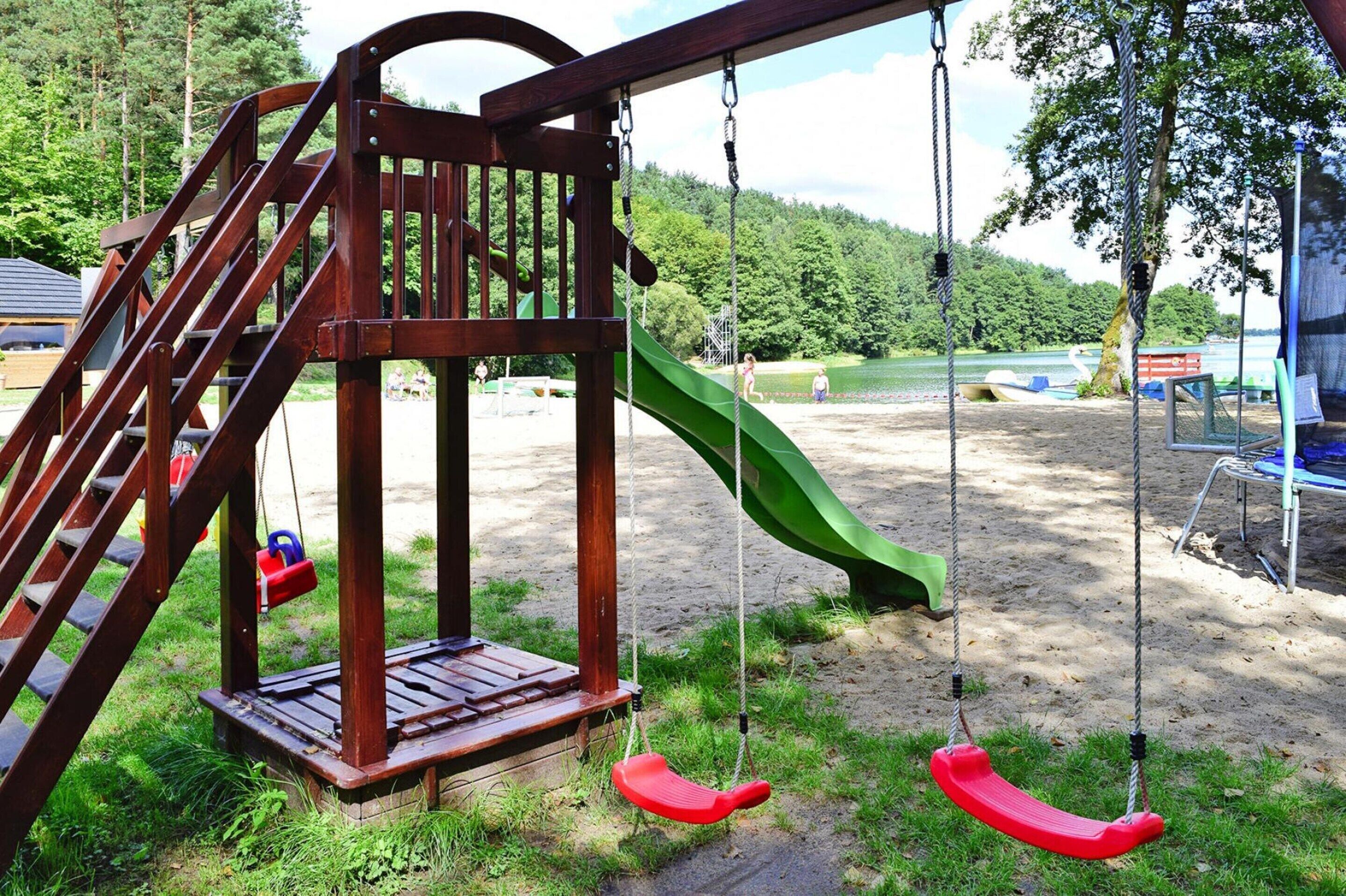 A playground with a wooden swing set, a green slide, and a sandy ground area.