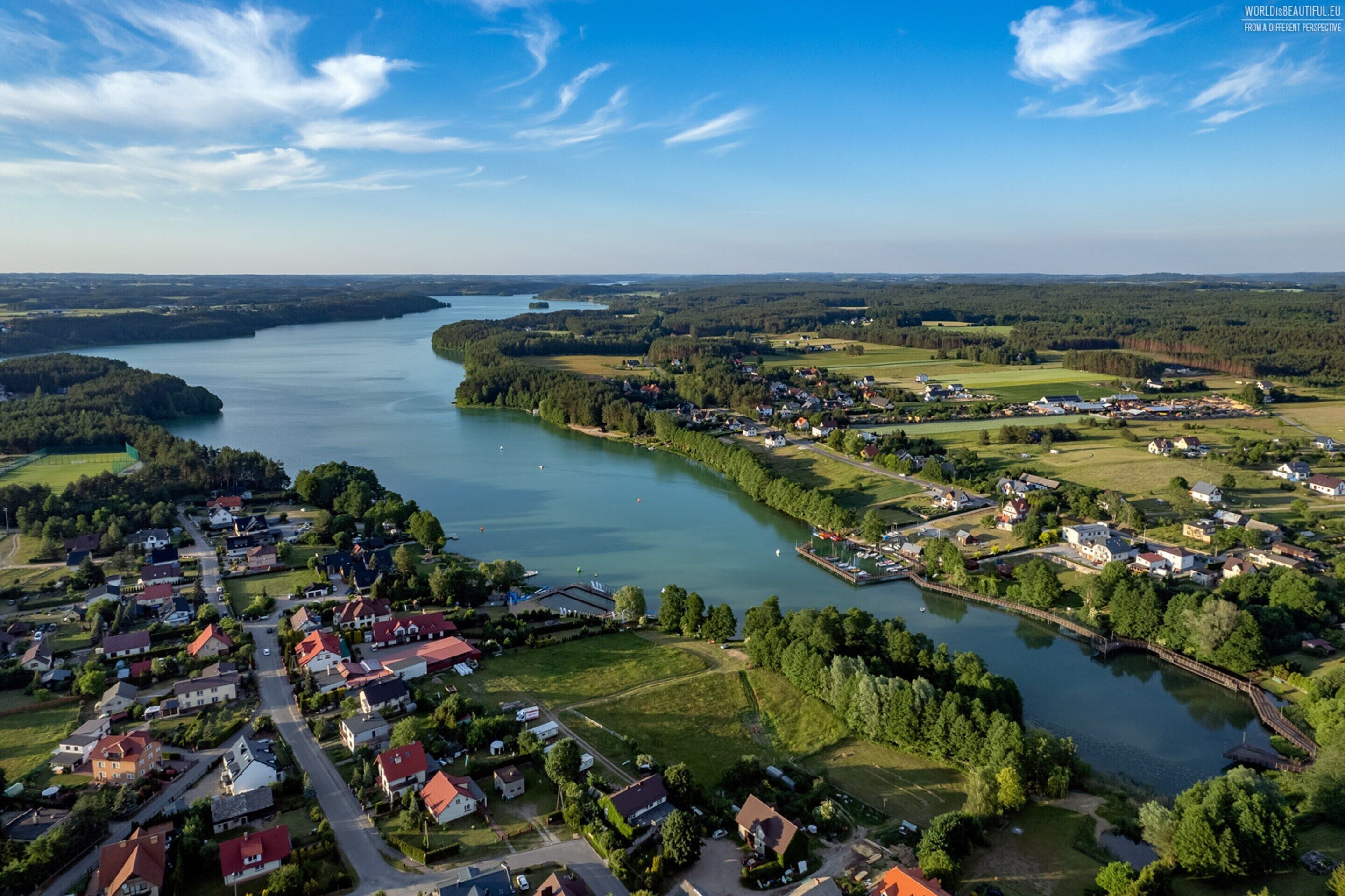 Vue aérienne d’une ville située au bord d’un lac, avec des immeubles résidentiels, une marina et une végétation luxuriante environnante.