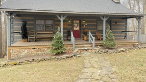 A log cabin with a porch, two small Christmas trees, and a stone pathway leading to the entrance. - Bearadise 3BR w/Loft Cabin w/ Game Room, Fire Pit & Resort Amenities (Terra Alta)