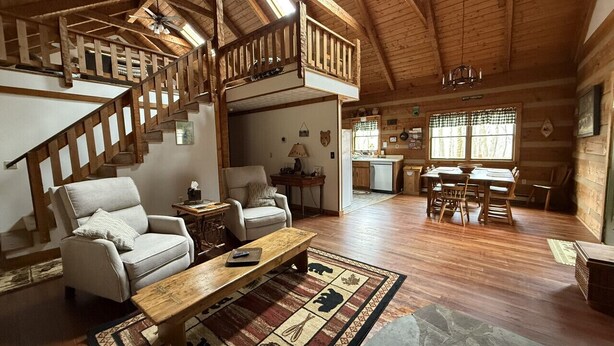 A spacious cabin interior with a wooden staircase, a dining area, and a kitchen. - Bearadise 3BR w/Loft Cabin w/ Game Room, Fire Pit & Resort Amenities (Terra Alta)