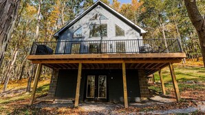 Eine Holzhütte mit einer Holzterrasse und einem Balkon, umgeben von Bäumen.