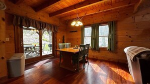 Interior de uma cabana de madeira com uma mesa de jantar, cadeiras, um banco e um sofá.