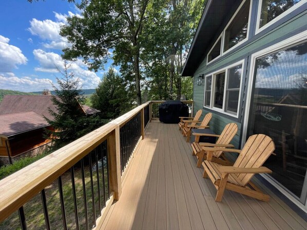 Une terrasse avec des rampes en bois, un barbecue et plusieurs chaises Adirondack.