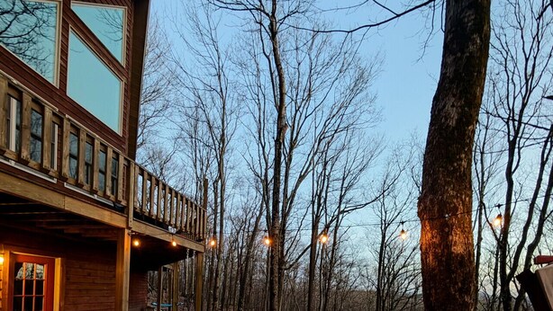 Un bain à remous avec des jets, entouré d’arbres et d’un bâtiment en bois doté d’un balcon.