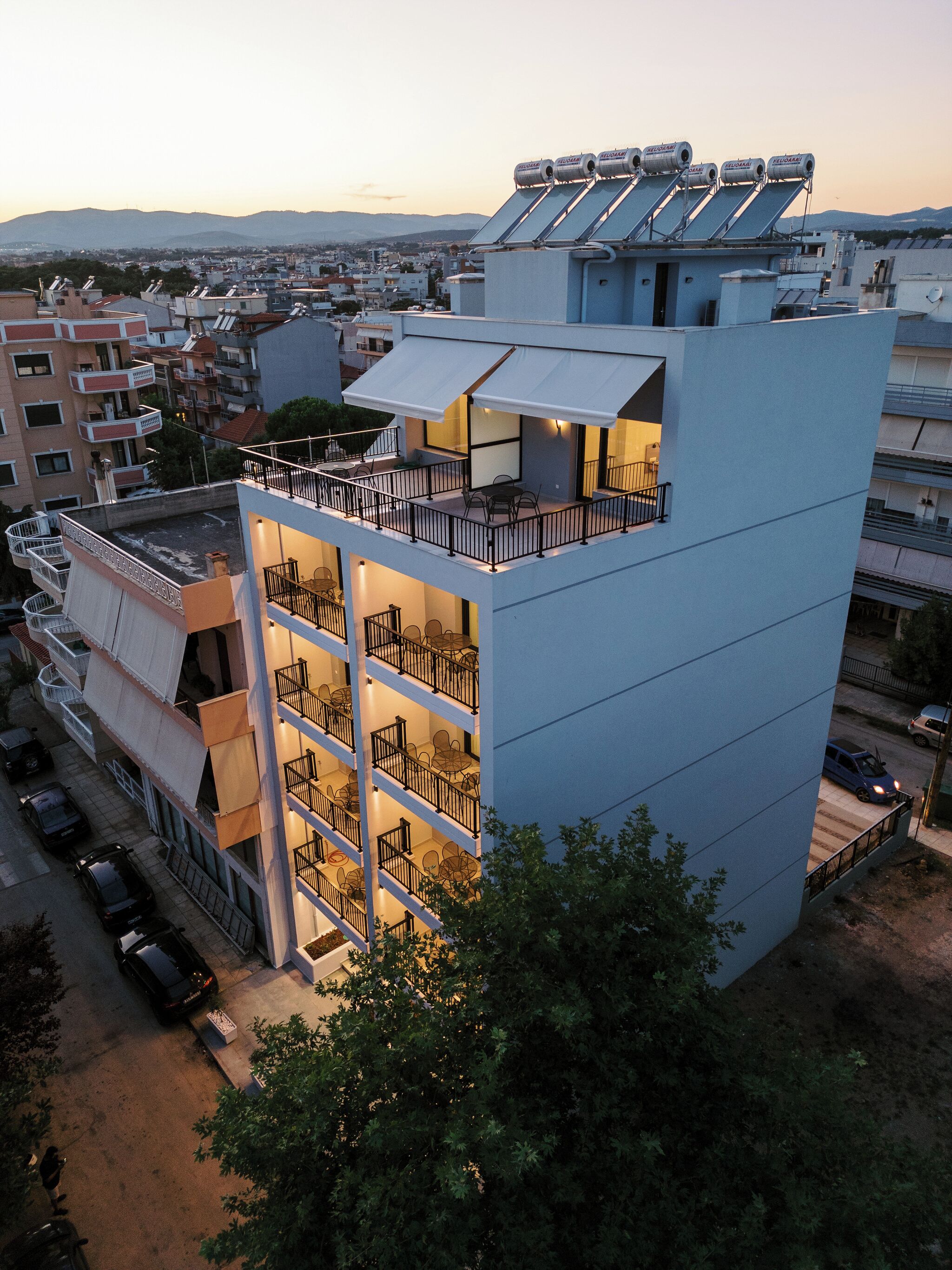 Un edificio moderno de varios pisos con terraza en la azotea, balcones y vistas a la ciudad.