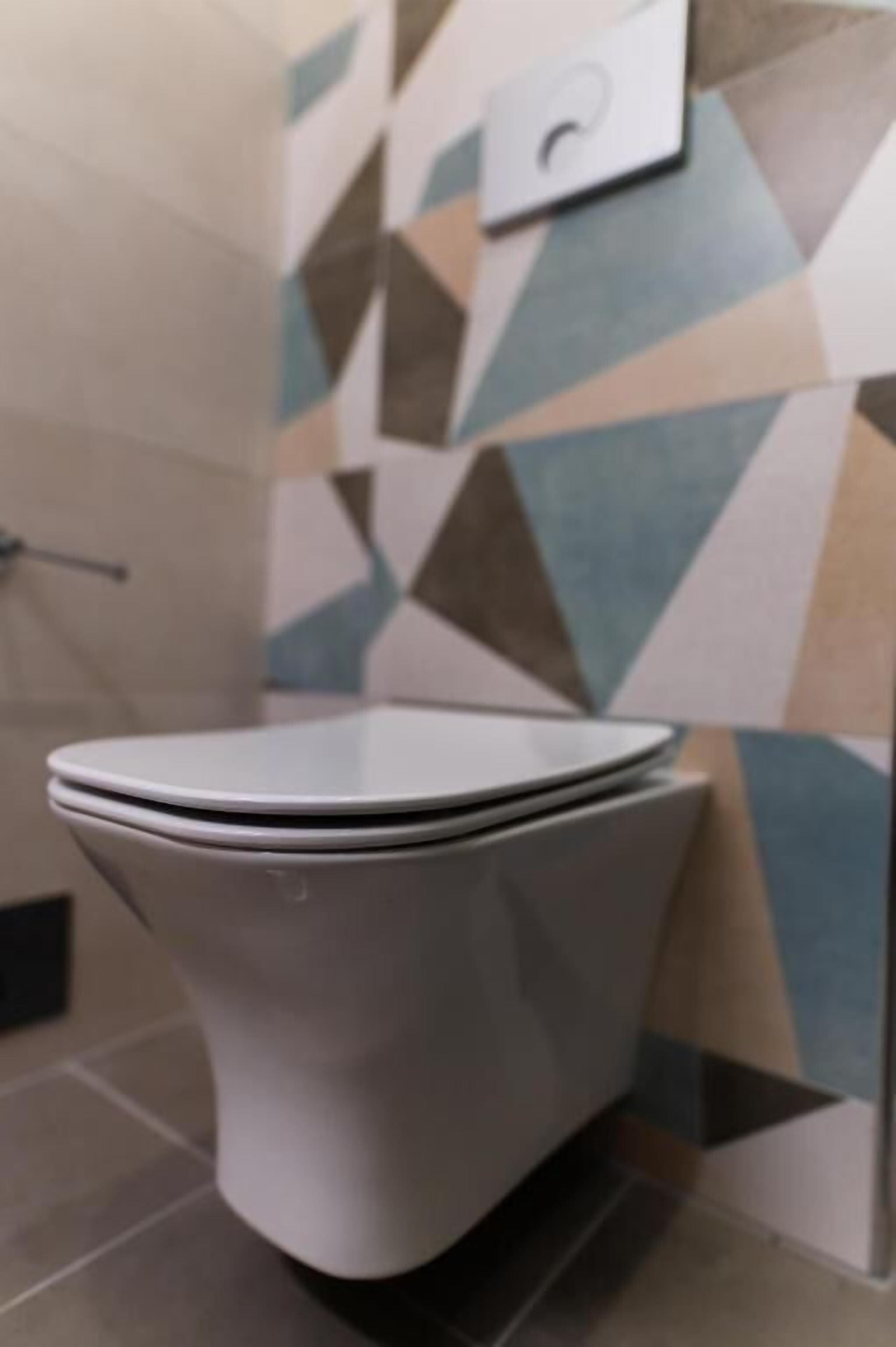 A toilet with a white seat and lid, positioned against a wall with a geometric tile pattern.