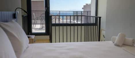 Una habitación de hotel con cama, ventana con vista al mar y balcón con sillas.