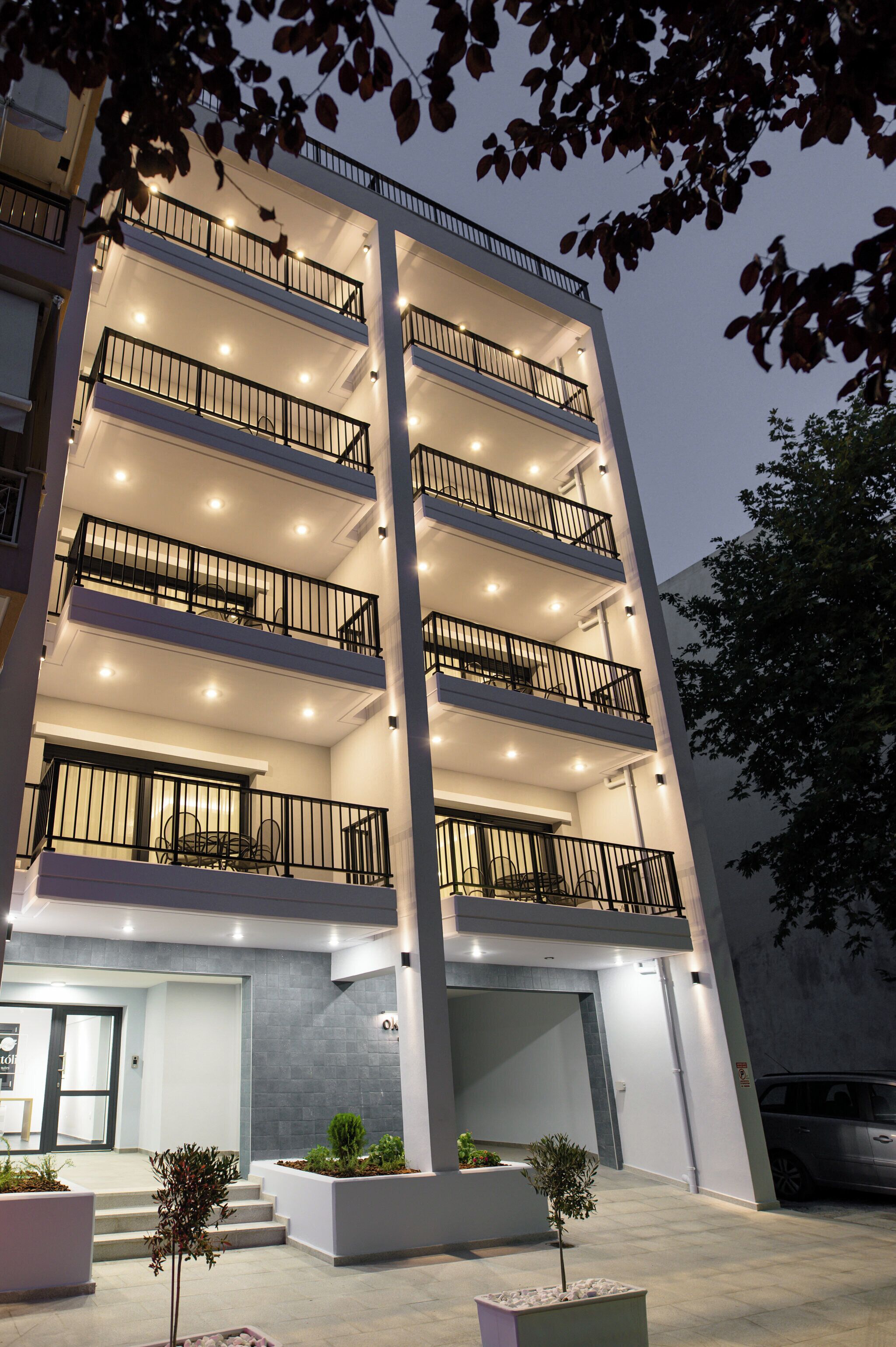 Un edificio de varios pisos con balcones, iluminación exterior y plantas en macetas.