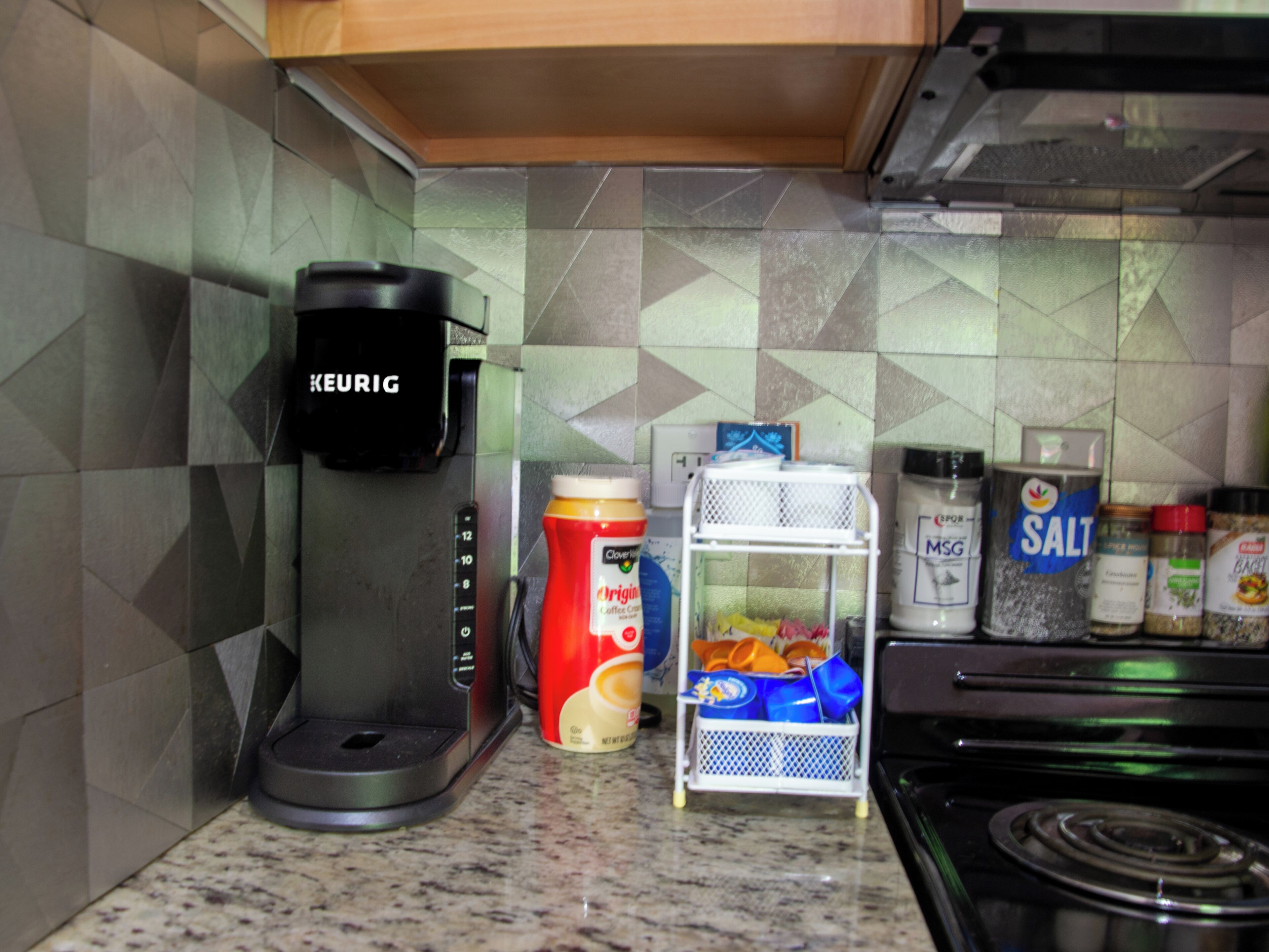 A kitchen with a Keurig coffee maker, a coffee cup, a spice rack, and a salt container.