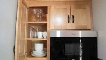 Uma cozinha com micro-ondas, armários de madeira e prateleiras com copos e louças.