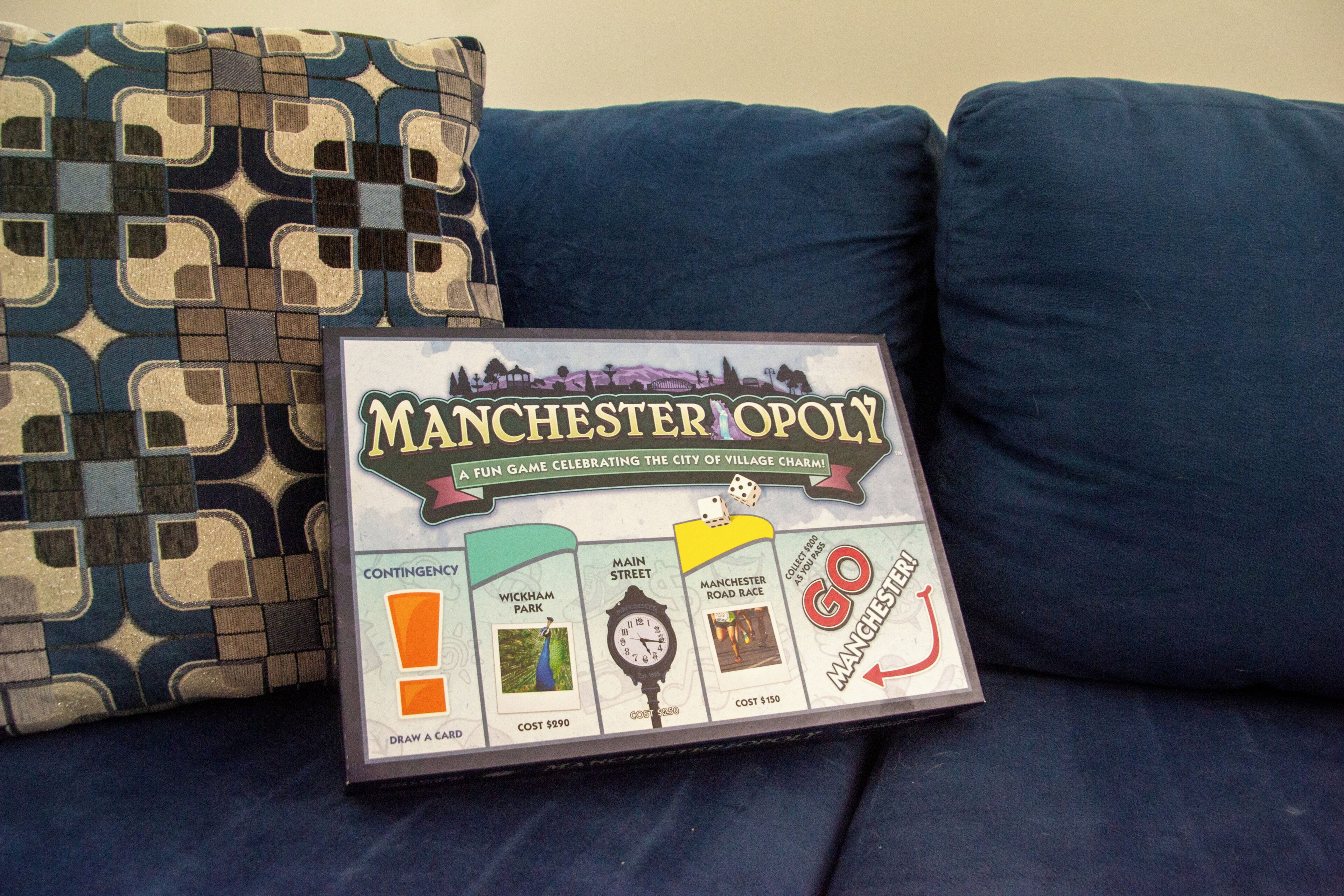 A board game titled 'Manchester Monopoly' on a blue couch with patterned pillows.
