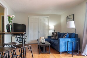 A living room with a TV, a sofa, a coffee table, a lamp, and a vase with flowers. - Peaceful pet friendly 1-bedroom with in unit laundry in enjoyable Manchester (Manchester)