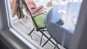 Udsigt fra et værelse til en balkon med et bord, en stol, et glas vin og et tæppe på stolen.
