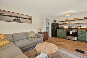Un salon moderne avec un canapé gris, une table basse ronde en bois et un tableau accroché au mur.