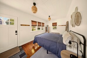A bedroom with a bed, a door, windows with blinds, a ceiling fan, and a wall-mounted light fixture.