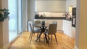 Una cocina moderna con armarios blancos, un área de comedor con una mesa redonda y sillas, y un ventanal que proporciona luz natural.