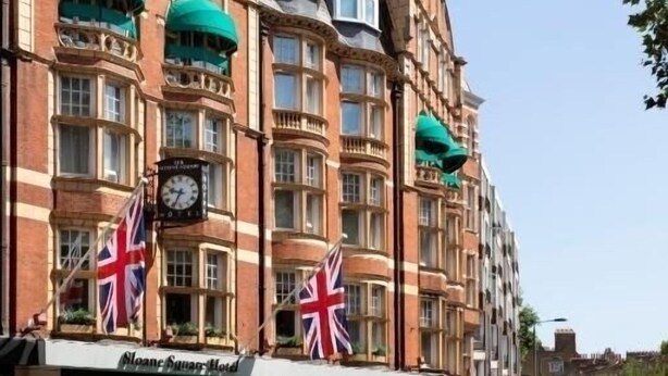 Un hotel histórico con banderas británicas, un reloj y un toldo verde.