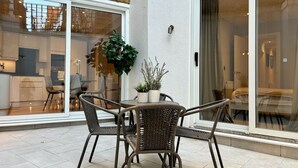 Un patio moderno con sillas de mimbre y una mesa, puertas correderas de vidrio que dan a un espacio habitable y una planta en maceta sobre la mesa.