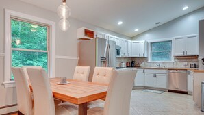 A modern kitchen with white cabinets, a stainless steel refrigerator, and a wooden dining table with chairs. - Cabin w/ Beach Access in Brant Lake: Dogs Welcome! (Brant Lake)