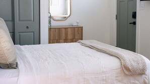 Una camera da letto con un letto, una cassettiera in legno, uno specchio e un lampadario.